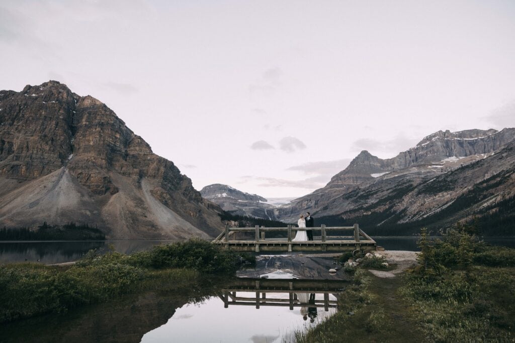 couple walking across bridge at bow lake in banff national park