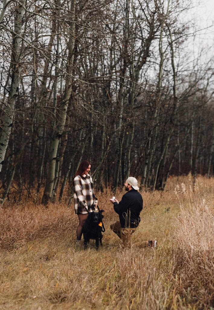 guy proposing to his now fiance at their family farm in the woods with their dog
